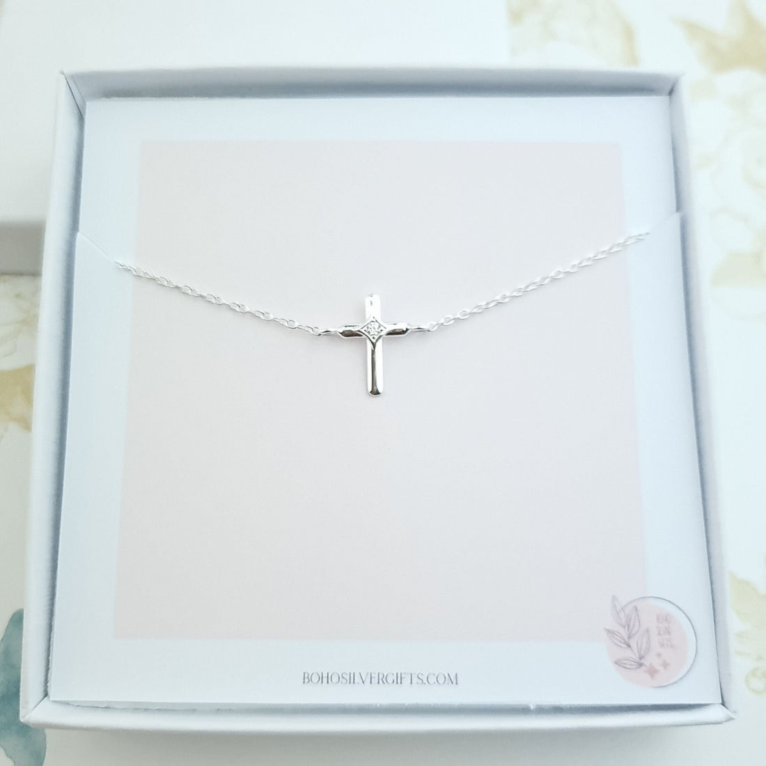 Sterling silver bracelet with a small cross charm featuring a diamond-cut centre, displayed on a white background.